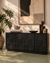 Load image into Gallery viewer, A modern black wooden console cabinet with a geometric block pattern, styled in a warm, sunlit room with a potted plant, books, and abstract wall art.