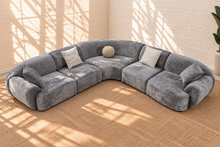 Load image into Gallery viewer, Aela curved sectional sofa upholstered in textured ash grey fabric with rounded corners, square arms, tight back, and five toss pillows.
