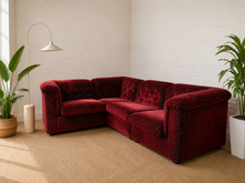 Load image into Gallery viewer, A deep burgundy velvet sectional sofa with a textured dotted pattern, styled in a bright room with a white brick wall, beige carpet, a floor lamp, and potted plants.