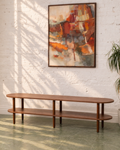 Load image into Gallery viewer, A mid-century modern wooden console table with two shelves, positioned against a white brick wall under a framed abstract painting.