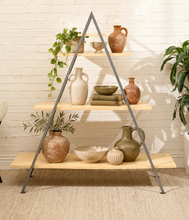 Load image into Gallery viewer, A three-tier wooden shelf with a gray metal A-frame structure, styled with ceramic vases, bowls, and green plants against a white brick wall.