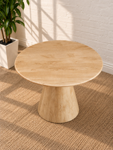 Load image into Gallery viewer, A round wooden coffee table with a natural light beige finish, set on a textured beige rug against a white brick wall with soft window shadows.