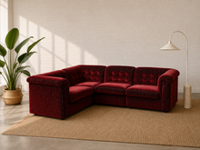 Load image into Gallery viewer, A deep burgundy velvet sectional sofa with tufted back cushions, styled in a modern living room setting on a beige jute rug with a potted plant and a floor lamp.