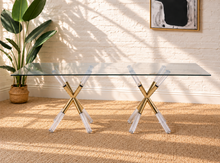 Load image into Gallery viewer, Flavia rectangular glass dining table with tempered glass top and sculptural X-shaped base in gold metal and clear acrylic.