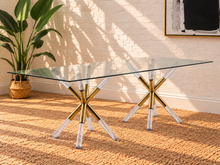 Load image into Gallery viewer, Flavia rectangular glass dining table with tempered glass top and sculptural X-shaped base in gold metal and clear acrylic.