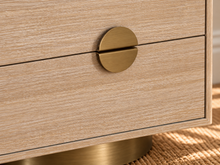 Load image into Gallery viewer, Jimena blonde oak two-drawer nightstand with brushed brass metal base and circular handle.