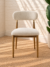 Load image into Gallery viewer, Kenna dining chair with off-white bouclé upholstered seat and rounded backrest, warm wood frame and brass-toned backrest caps.