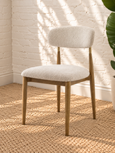 Load image into Gallery viewer, Kenna dining chair with off-white bouclé upholstered seat and rounded backrest, warm wood frame and brass-toned backrest caps.
