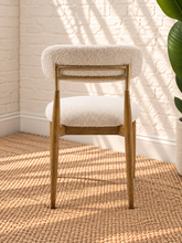 Load image into Gallery viewer, Kenna dining chair with off-white bouclé upholstered seat and rounded backrest, warm wood frame and brass-toned backrest caps.