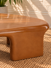 Load image into Gallery viewer, Klarisse caramel high-gloss concrete coffee table with elongated rounded top and sculptural waterfall-style supports.