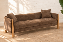 Load image into Gallery viewer, Lexi three-seat sofa upholstered in textured taupe brown fabric with exposed solid wood legs, square arms, and two matching toss pillows.