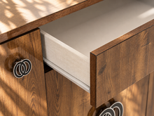 Load image into Gallery viewer, Maren Italian four-door credenza with gloss-finished rovere wood grain, center drawer, and chrome and black C-shaped hardware.