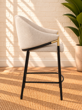 Load image into Gallery viewer, Image 3 of 4: Melani upholstered counter stool in Pearl Oat linen with curved back, black metal legs, gold accents, and footrest