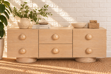 Load image into Gallery viewer, Norris Blonde Oak buffet credenza with oversized orb knobs, central drawers, cabinet storage, and rounded pedestal base