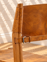 Load image into Gallery viewer, Nova counter stool in natural brown genuine leather with a tall teak wood frame, leather seat and backrest, footrest, and buckle strap detail.