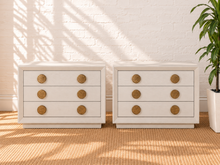 Load image into Gallery viewer, Pair of Phoebe three-drawer nightstands in cream white ash veneer with textured round golden metal handles and recessed plinth bases.