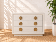 Load image into Gallery viewer, Phoebe three-drawer nightstand in cream white ash veneer with six round textured golden metal handles and recessed plinth base.