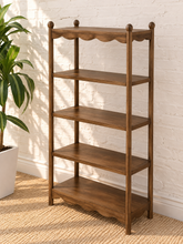 Load image into Gallery viewer, Image 3 of 5: A 4-tier wooden shelving unit with a warm medium-brown finish, featuring scalloped edges on the top and bottom shelves, set against a white brick wall next to a potted plant.