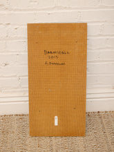 Load image into Gallery viewer, A square tan cardboard or paperboard panel standing upright against a white painted brick wall, with handwritten text reading 'Barnsdoll 2019 A. Donlan' and a small white label near the bottom.