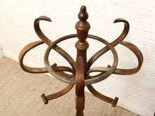 Load image into Gallery viewer, A vintage wooden coat rack with a central turned post, a circular ring, and four curved hanging arms, photographed indoors against a white brick wall and beige carpet.