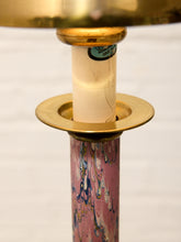 Load image into Gallery viewer, Close-up of a table lamp featuring a pink marbled glass column with blue and gold veining, a gold-finished collar, and a cream-colored candle-style bulb inside a brass socket.