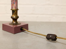 Load image into Gallery viewer, A close-up of a vintage table lamp featuring a dusty rose pink square base, a brass-colored neck with a colorful marbled pink and blue glass shade, and a tan cord with a dark brown switch.
