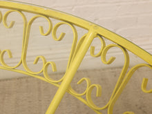 Load image into Gallery viewer, Close-up of a yellow metal frame with decorative scrollwork and a curved top rail, photographed against a light brick wall and neutral floor.