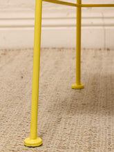Load image into Gallery viewer, Close-up of a yellow metal table frame with round feet on a woven beige rug against a white wall.