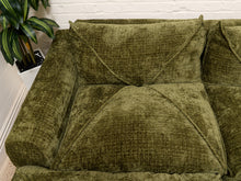 Load image into Gallery viewer, An olive green textured fabric sofa with matching back and seat cushions, shown in a home setting against a white brick wall with a potted plant on the left.