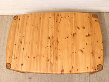 Load image into Gallery viewer, A rectangular pine wood coffee table viewed from directly above, showing natural wood grain, knots, and rounded corners with protective caps, set on a textured beige rug against a white brick wall.