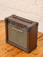 Load image into Gallery viewer, A vintage Behringer CH-1120X18 electric guitar amplifier with a brown leatherette body, black handle, and beige speaker grille, sitting on a wooden floor against a white brick wall.