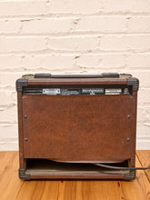 Load image into Gallery viewer, A vintage Behringer LA-1000A tube amplifier with a brown leatherette front cover, set on a wooden floor against a white brick wall.