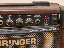 Load image into Gallery viewer, Close-up of a vintage Ringer Ultracoustic AT108 guitar amplifier showing the brown wood-grain cabinet, black control knobs, speaker grille, and power switch.