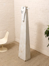 Load image into Gallery viewer, A tall, tapered white wooden sculpture with a distressed finish stands in a corner of a room with a white brick wall, beige carpet, a white molded chair, and a green plant.