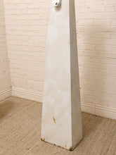 Load image into Gallery viewer, A tall, tapered white wooden post or column with a weathered, rustic finish, standing on a beige woven rug against a white brick wall.