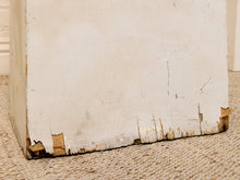 Load image into Gallery viewer, A close-up of a distressed white painted wooden box corner showing chipped paint, wood grain, and wear on a beige woven rug.