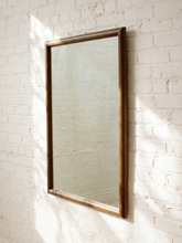 Load image into Gallery viewer, A tall rectangular wall mirror with a rustic bronze-brown wooden frame, mounted on a white painted brick wall with soft sunlight and leaf shadows.