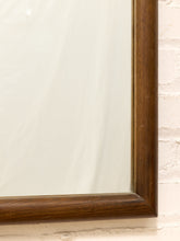 Load image into Gallery viewer, Close-up of a rectangular wall mirror with a thick dark brown wooden frame, mounted against a white brick wall.