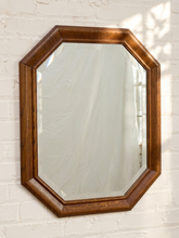 Load image into Gallery viewer, An octagonal wall mirror with a warm medium-brown wooden frame, mounted on a white painted brick wall.