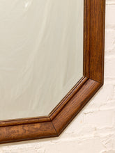 Load image into Gallery viewer, Close-up of a hexagonal mirror with a thick, dark brown wooden frame, resting against a white brick wall.