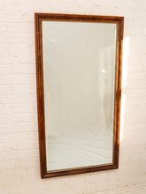 Load image into Gallery viewer, A tall rectangular wall mirror with a dark brown wooden frame, mounted on a white painted brick wall.
