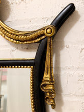Load image into Gallery viewer, Close-up of an ornate black and gold mirror frame with decorative gold scrollwork and bead detailing, mounted against a textured off-white wall.