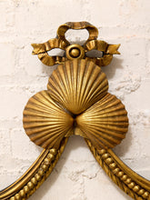 Load image into Gallery viewer, An ornate gold-toned decorative wall piece featuring two large scallop shell motifs, a ribbon-like top element, and rope-textured lower arms, mounted against a white painted brick wall.