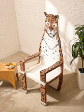 Load image into Gallery viewer, A creatively shaped wooden chair designed to look like a leopard, featuring a white body with black spots and a detailed leopard face on the backrest, set in a bright room with a white brick wall, beige carpet, and a small side table.