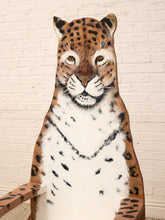 Load image into Gallery viewer, A hand-painted wooden chair shaped like a leopard, featuring a realistic leopard face on the backrest and spotted brown wood arms, set against a white brick wall.