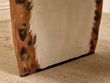Load image into Gallery viewer, A close-up of a rustic wooden board or furniture leg with a distressed finish, showing a cream-painted center and weathered brown wood edges with dark blackened spots, standing on a beige woven rug.