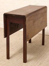 Load image into Gallery viewer, A dark brown wooden drop-leaf table with a rectangular top and four legs, shown on a textured beige rug against a white brick wall.