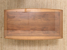 Load image into Gallery viewer, A rectangular wooden display case or cabinet with a clear glass top and a warm medium-brown wood frame, photographed from above on a woven beige rug.