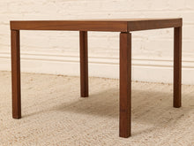 Load image into Gallery viewer, A square wooden side table with a medium brown finish and four straight legs, shown on a textured beige rug against a white brick wall.
