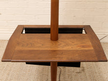 Load image into Gallery viewer, Close-up of a mid-century modern wooden side table with a square top, thick wood pedestal pole, and black storage compartment underneath, set against a white brick wall and beige carpet.